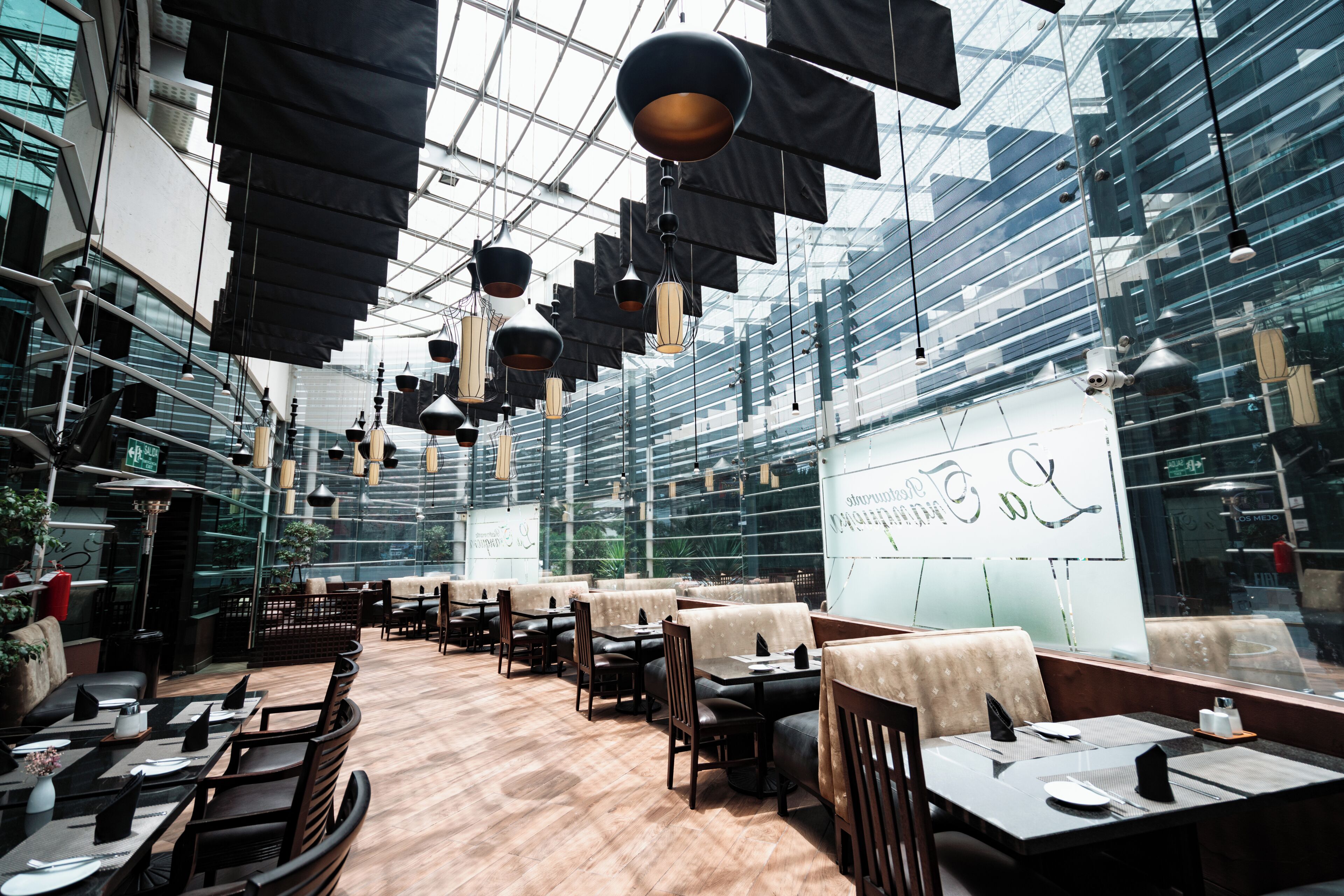 A modern restaurant with high ceilings and hanging pendant lights. Tables are arranged in a spacious layout with cushioned seating.