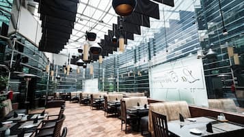 A modern restaurant with high ceilings and hanging pendant lights. Tables are arranged in a spacious layout with cushioned seating.