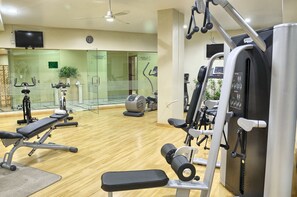 Un gimnasio con equipo de ejercicio variado, un televisor en la pared y un reloj.