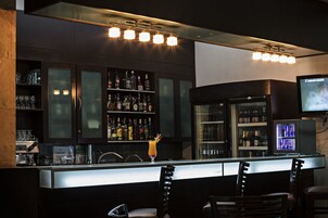 A bar area with a counter, bar stools, shelves with bottles, and a television screen.