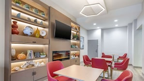 Un comedor moderno con sillas rojas y una mesa de madera, rodeado de estanterías con objetos decorativos y un televisor de pantalla plana.