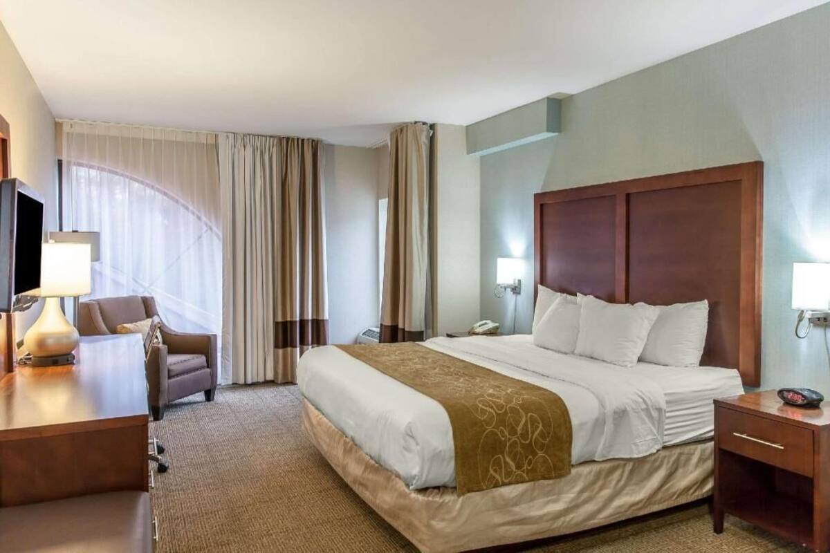 Una habitación de hotel con cama, mesita de noche, lámpara, silla y escritorio.