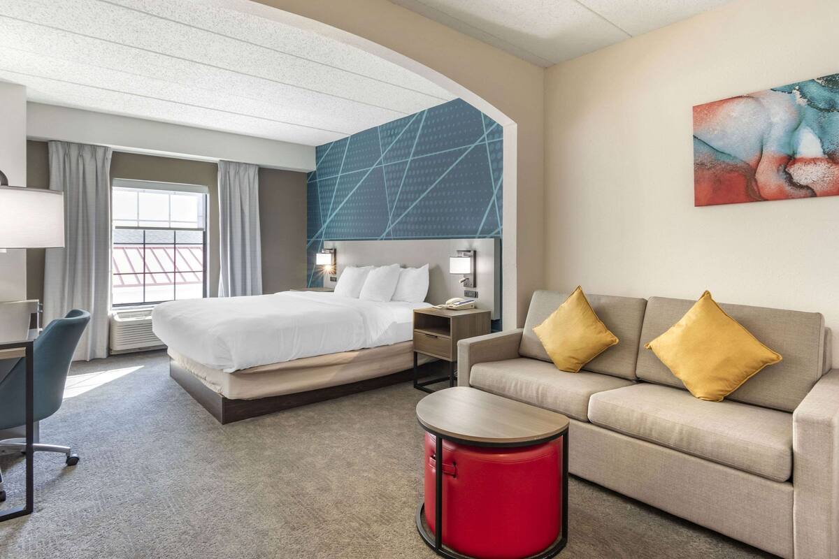 Una habitación de hotel con cama, sofá, escritorio y una mesita auxiliar roja.