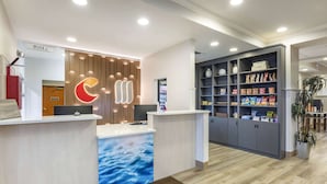 Zona de recepción con diseño moderno, que incluye un mostrador de recepción con un fondo con motivos de olas, un reloj digital y un estante con aperitivos.