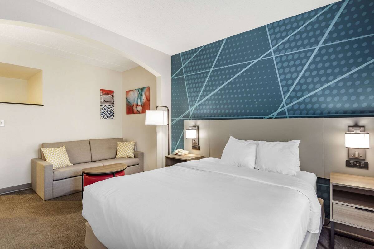 Una habitación de hotel con una cama grande, un sofá, una mesita y una pared con un diseño geométrico.