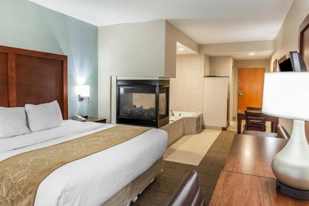 Una habitación de hotel con cama, televisión, chimenea, baño y zona de comedor.