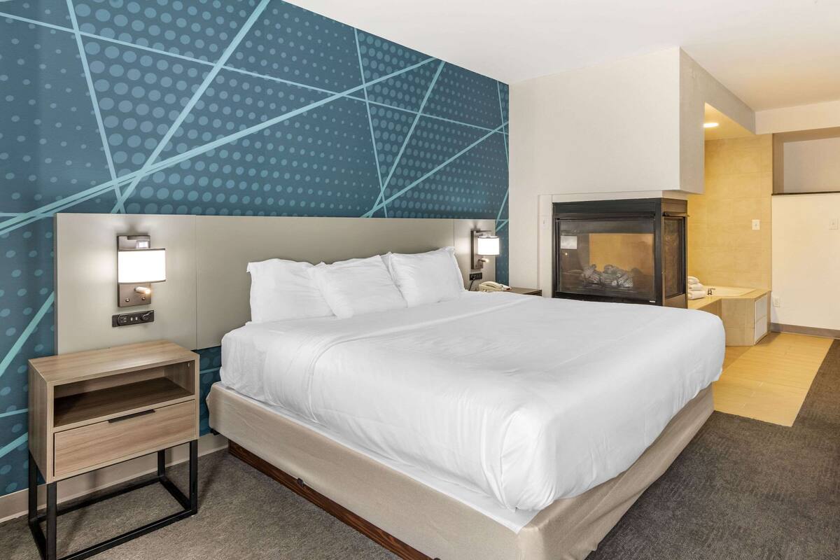 Habitación de hotel con una cama grande, mesitas de noche con lámparas, chimenea empotrada y una pared con estampado azul.