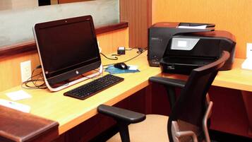 A wooden desk with a laptop, a desktop computer, a printer, and a chair.