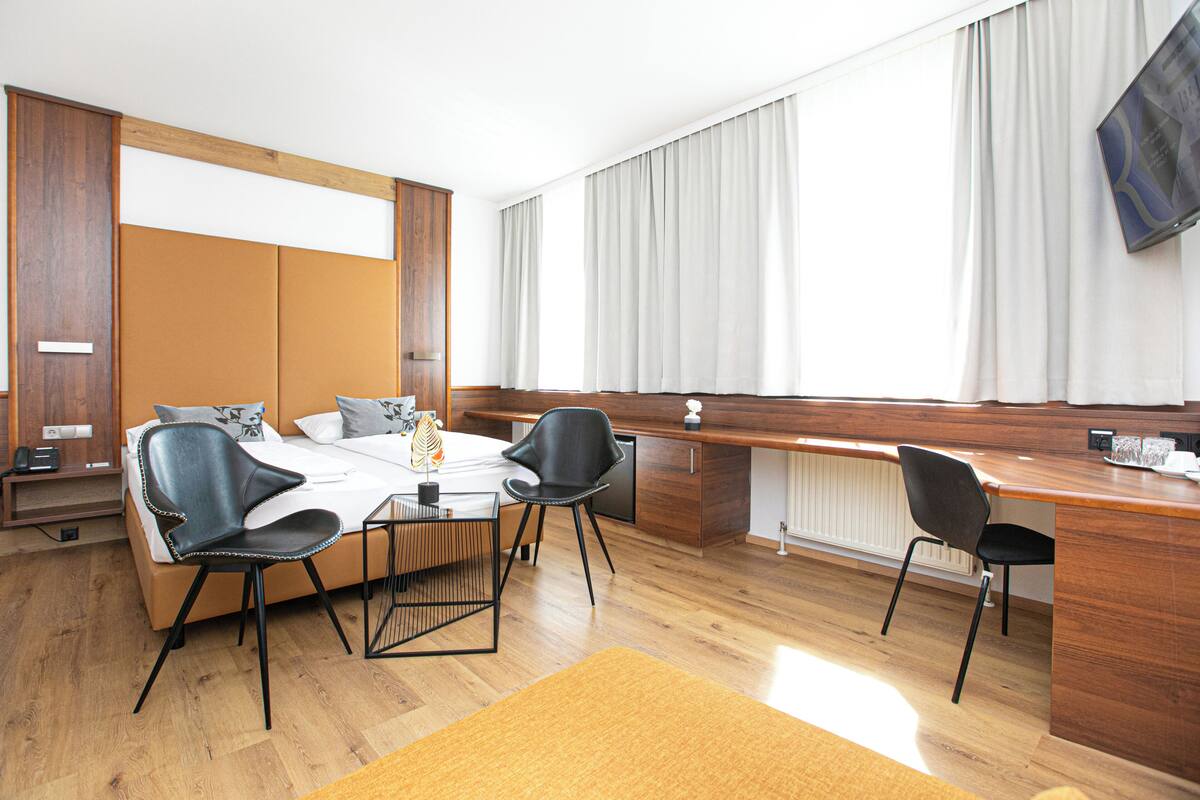 A modern hotel room with a bed, a desk, a chair, and a dining table.