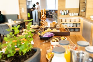 Un bufé de desayuno con panes, bollería y frutas variadas.