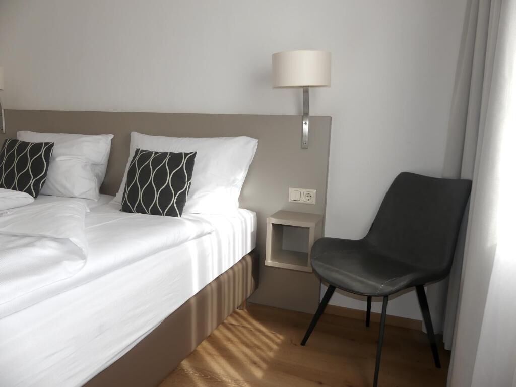 A hotel room with a bed, two pillows, a nightstand, a lamp, and a chair.