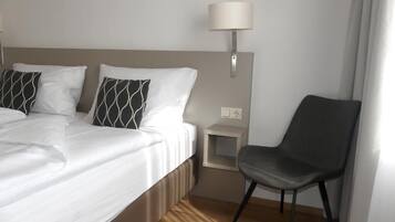 A hotel room with a bed, two pillows, a nightstand, a lamp, and a chair.