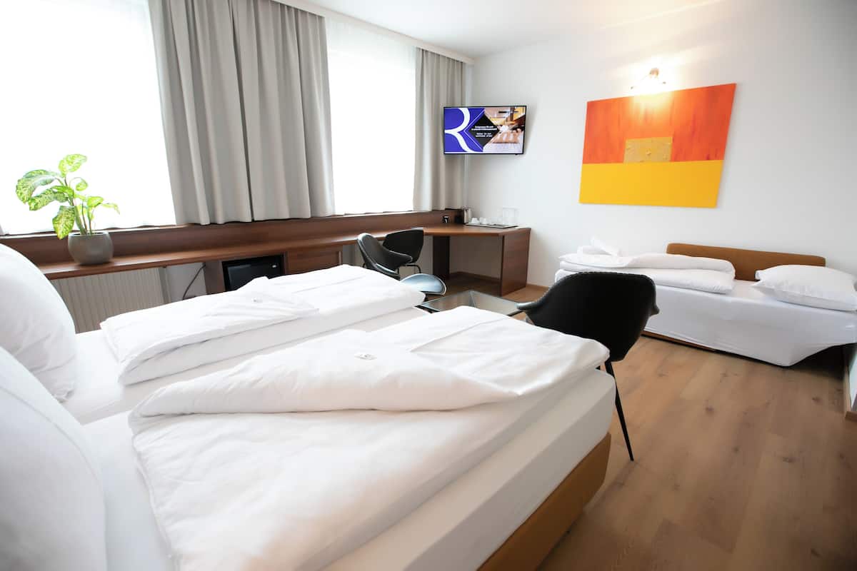 A hotel room with a bed, a desk, a chair, a TV, and a plant.