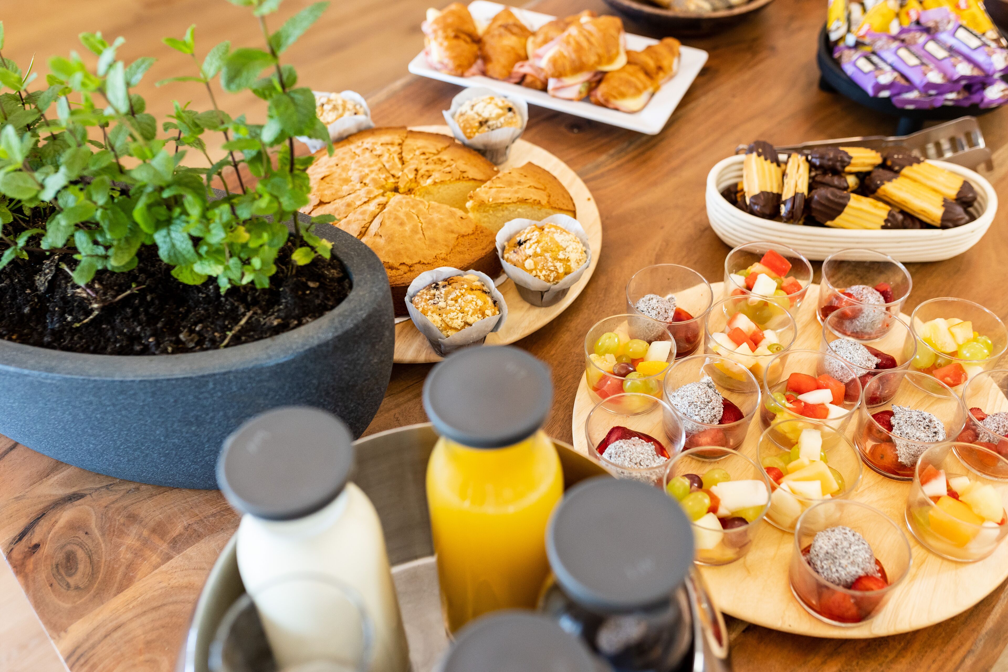 Una mesa con diversos alimentos, incluyendo pasteles, una bandeja de frutas y una botella de jugo.