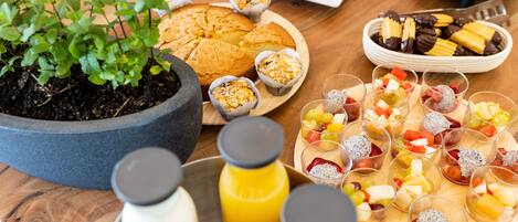 Una mesa con diversos alimentos, incluyendo pasteles, una bandeja de frutas y una botella de jugo.