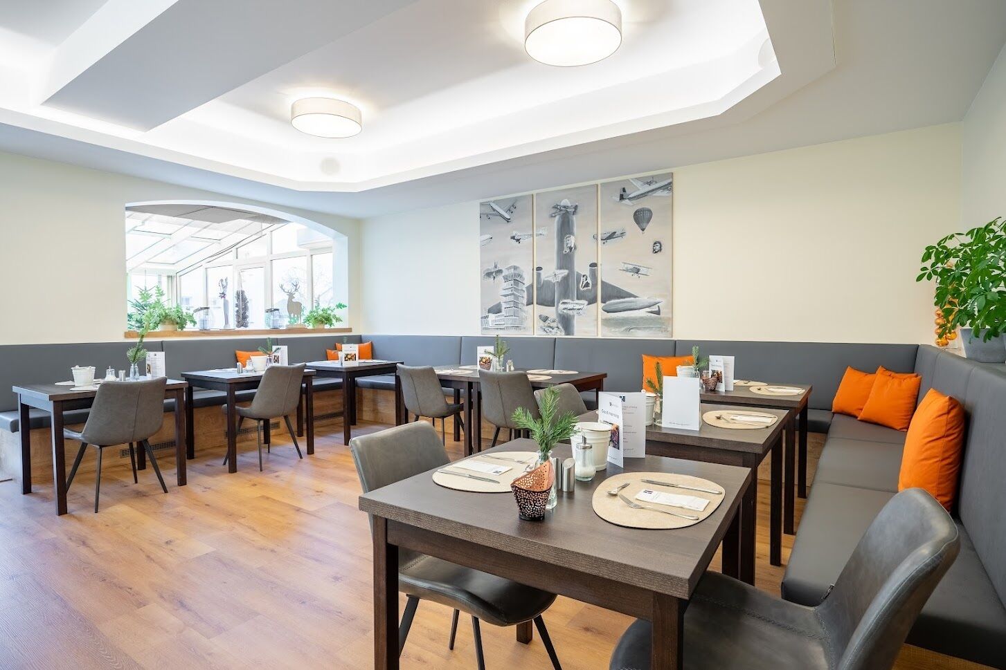 A modern dining area with multiple tables and chairs, a large window with a view, and a wall with aviation-themed artwork.