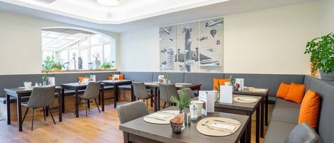A modern dining area with multiple tables and chairs, a large window with a view, and a wall with aviation-themed artwork.