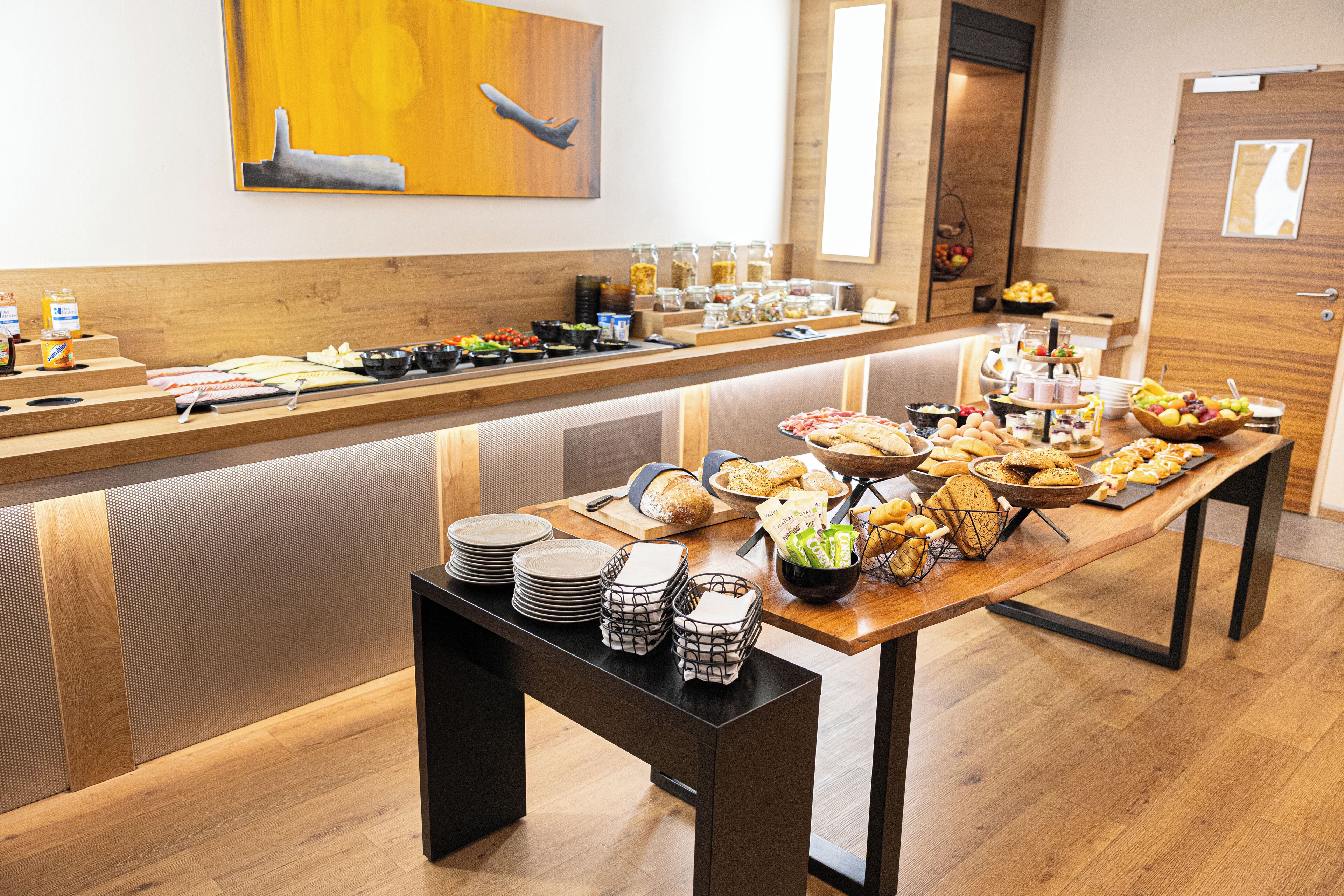 A buffet setup with various food items, plates, and serving utensils on a wooden table.