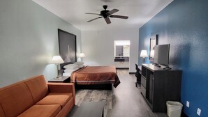 A hotel room with a bed, a sofa, a desk, a TV, and a ceiling fan. - Scottish Inns & Suites Forney/East Dallas (Forney)