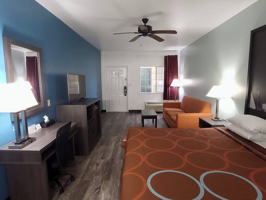 Habitación de hotel con cama, escritorio, silla, televisor, ventilador de techo y ventana con cortinas.