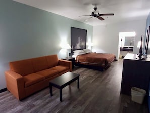 A hotel room with a sofa, a bed, a desk, a ceiling fan, and a bathroom visible through an open door.
