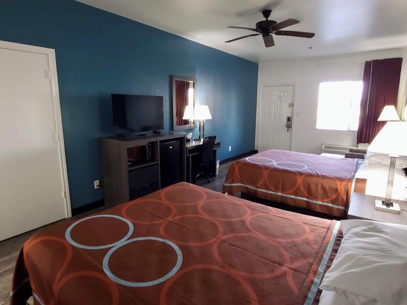 Habitación de hotel con dos camas, televisión, escritorio y ventilador de techo.