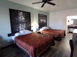 Quarto de hotel com duas camas, um ventilador de teto, uma pintura grande e um banheiro visível por uma porta aberta.