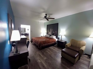 A hotel room with a bed, two bedside tables, a desk, a chair, a ceiling fan, and a large window.