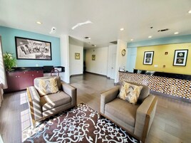 A reception area with a blue wall, a framed welcome sign, a reception desk, and two sofas with patterned cushions.