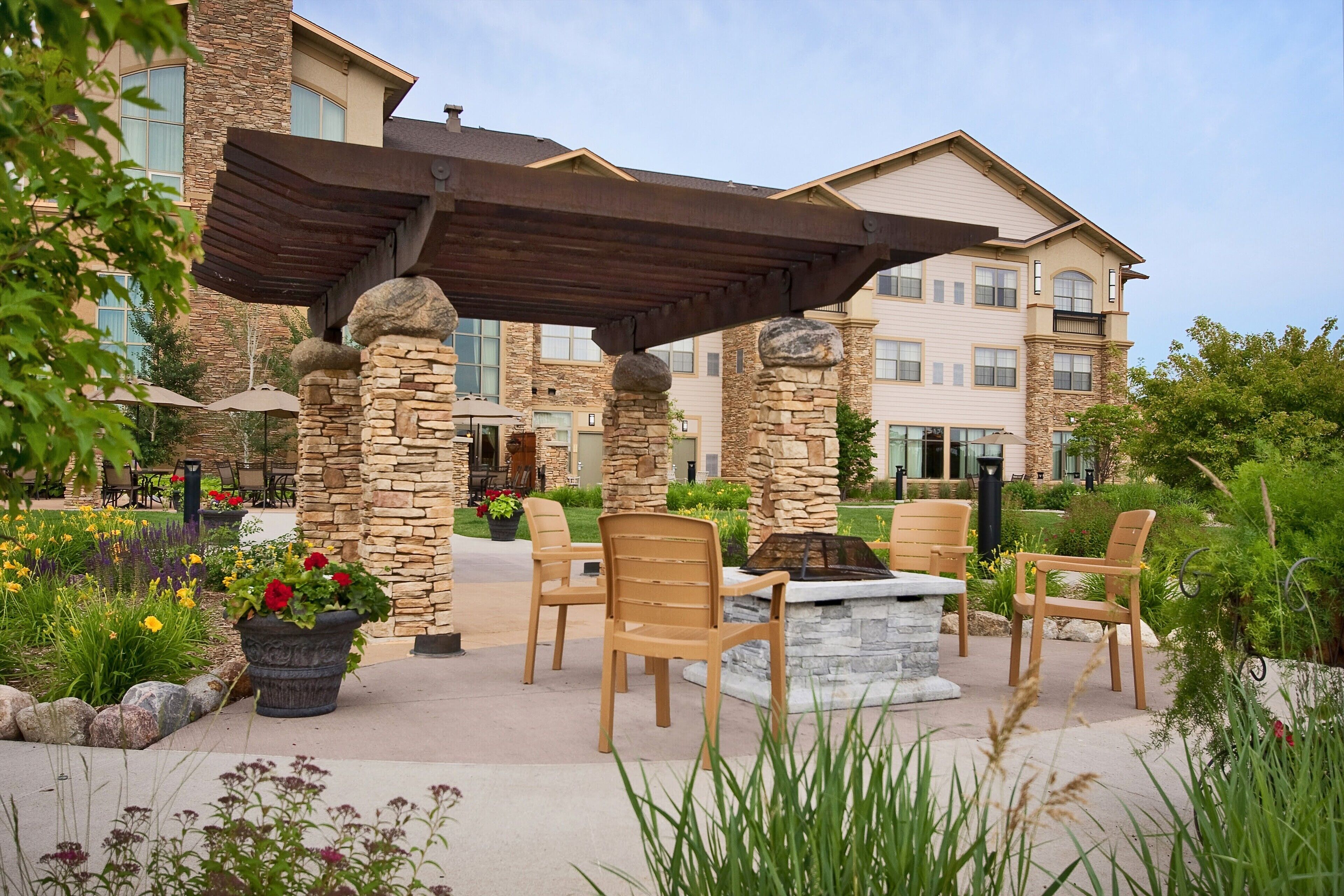 An outdoor patio area with stone pillars, wooden chairs, and a fire pit.