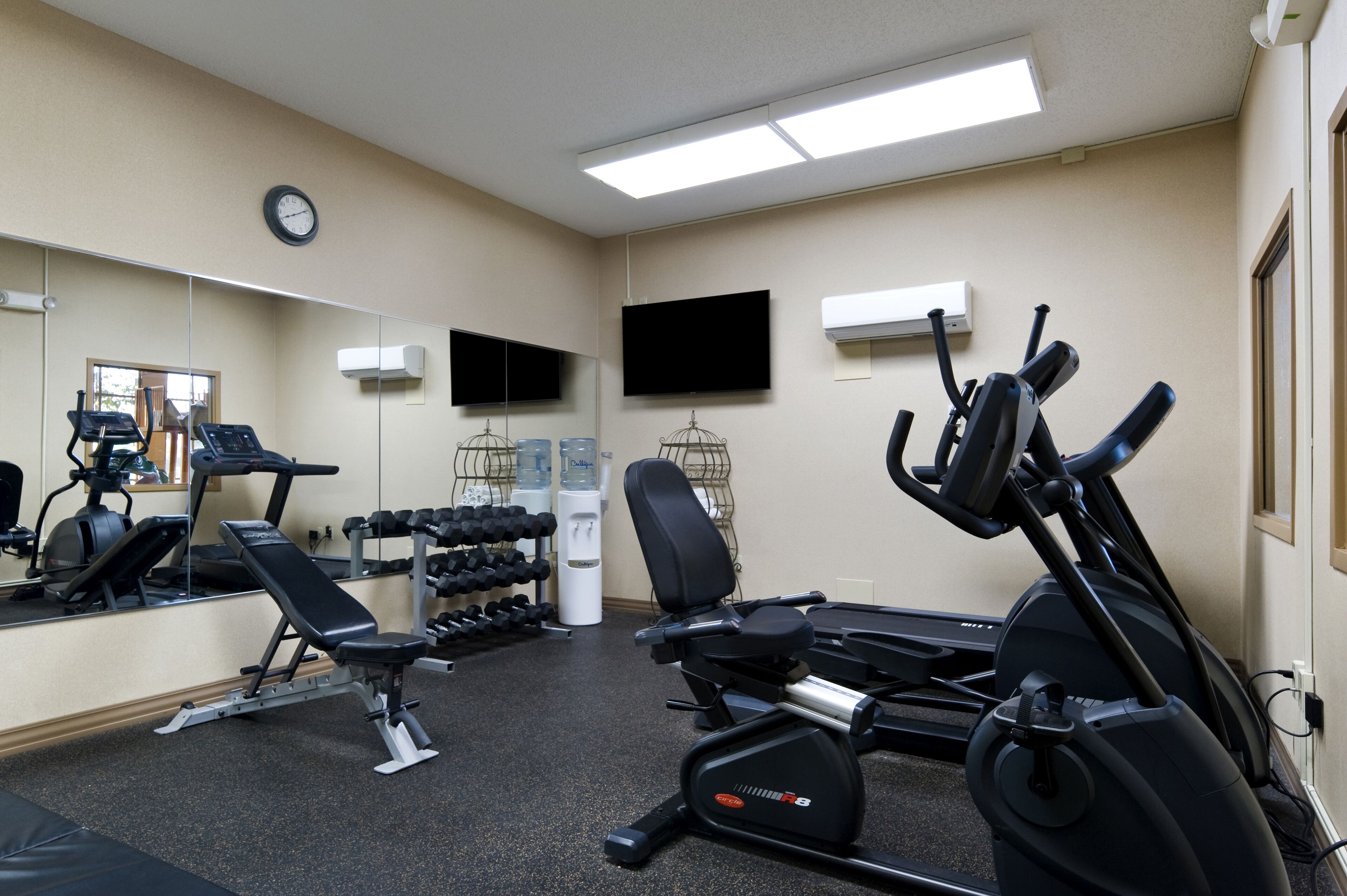 Une salle de sport équipée de matériel d’exercice, d’un miroir, d’une horloge et d’un téléviseur.