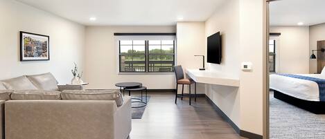 Et moderne hotelværelse med sofa, skrivebord, stol, seng, fjernsyn og vindue med udsigt.