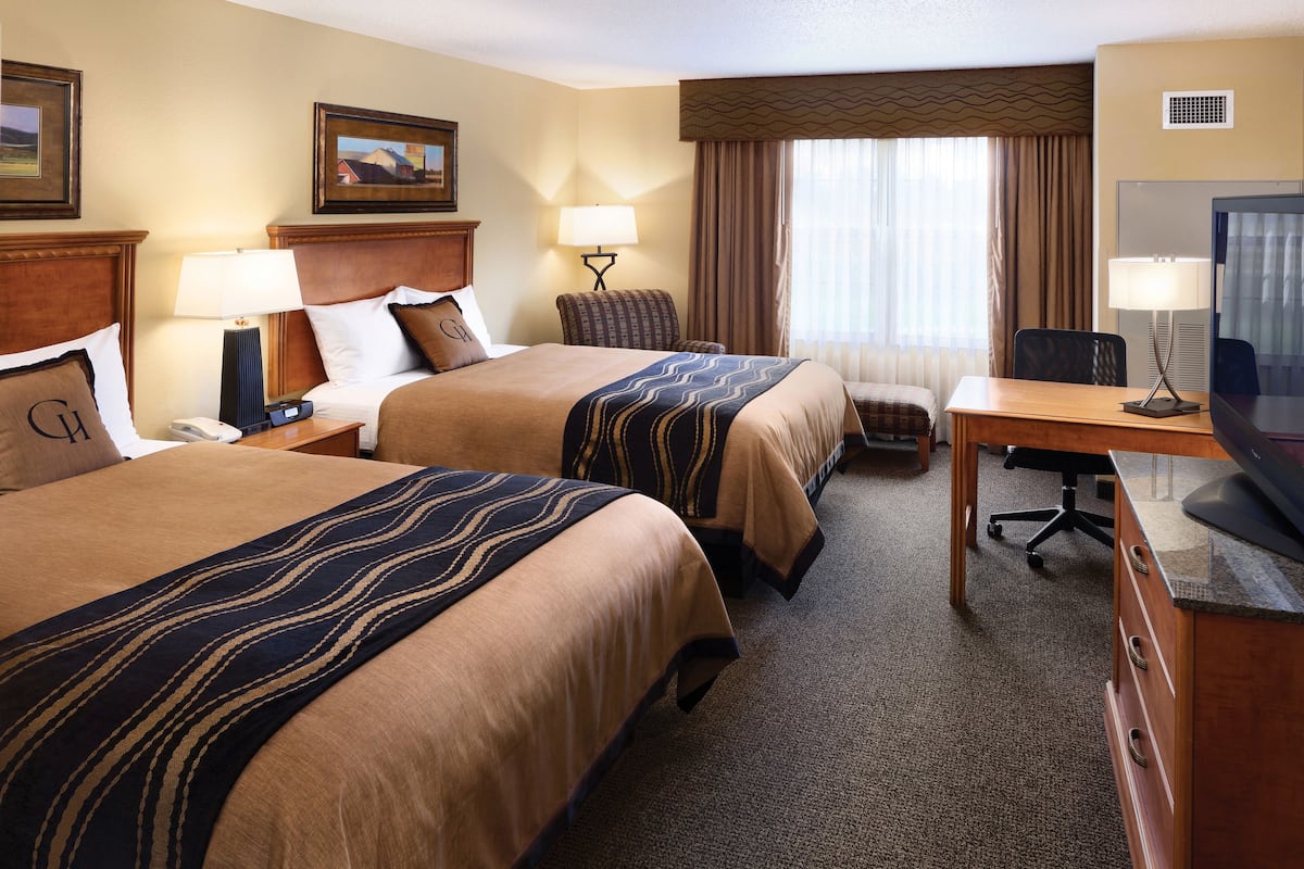 Une chambre d’hôtel avec deux lits, un bureau, une chaise, une télévision et une fenêtre avec des rideaux.
