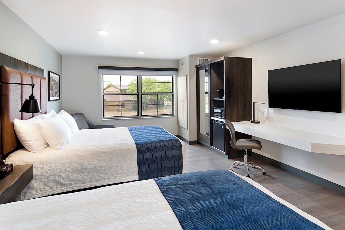 Une chambre d’hôtel avec deux lits, un bureau, une chaise, une télévision et une grande fenêtre.