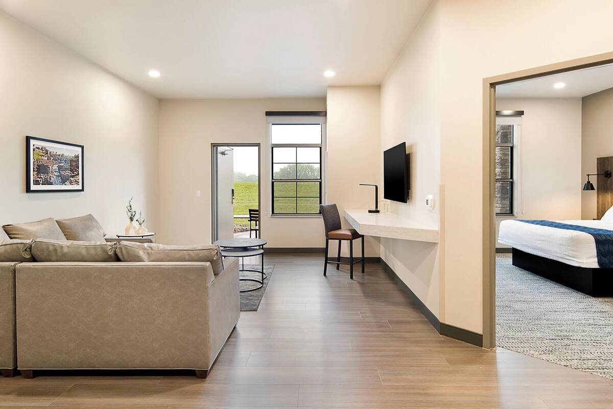 Une chambre d’hôtel moderne équipée d’un canapé, d’un bureau, d’une chaise, d’un lit, d’une télévision et d’une grande fenêtre.