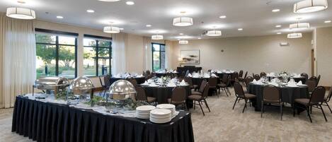 A banquet hall with round tables, chairs, and a buffet setup.