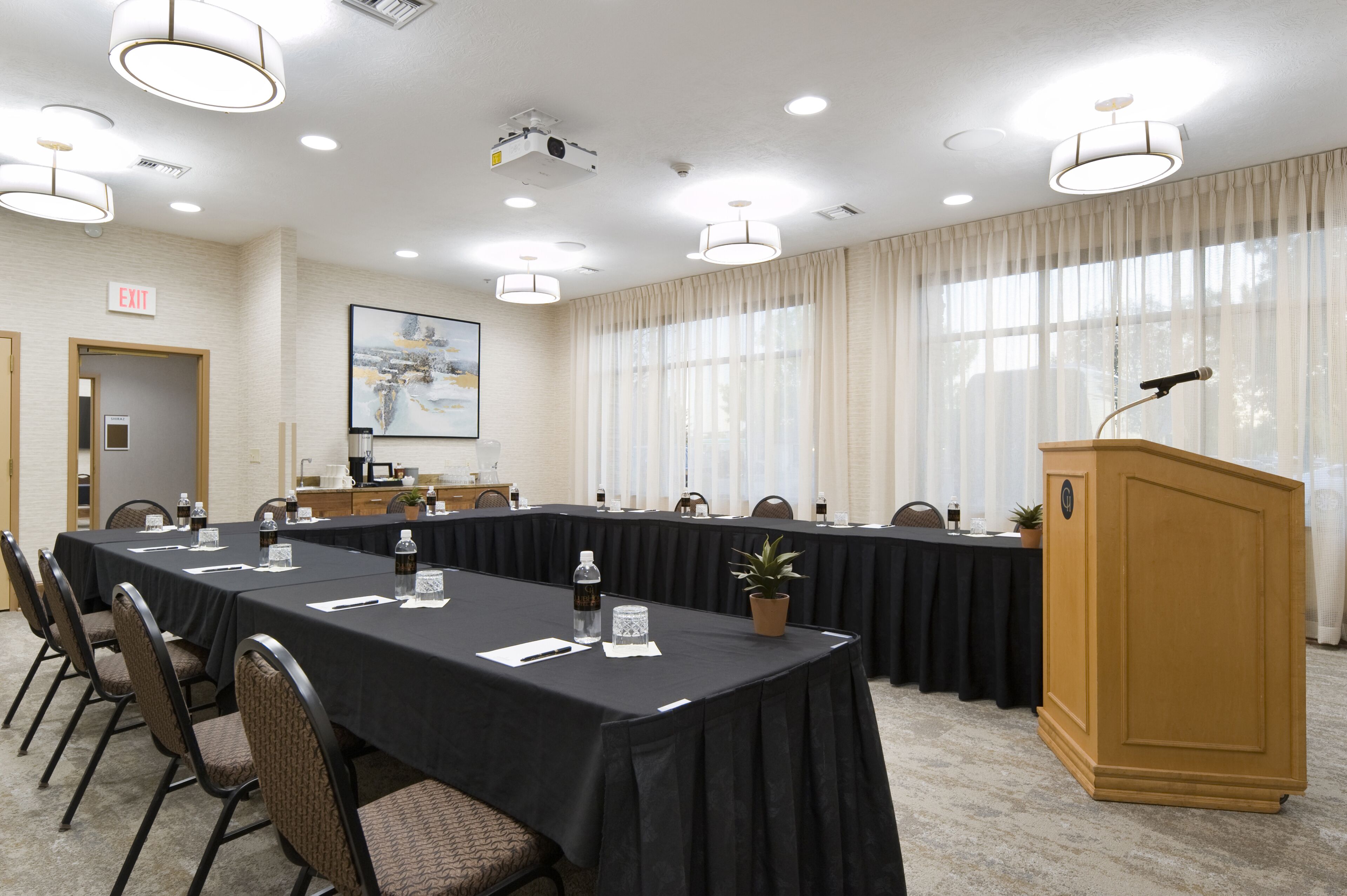 Un salón de conferencias con una larga mesa, sillas, un atril y un proyector.