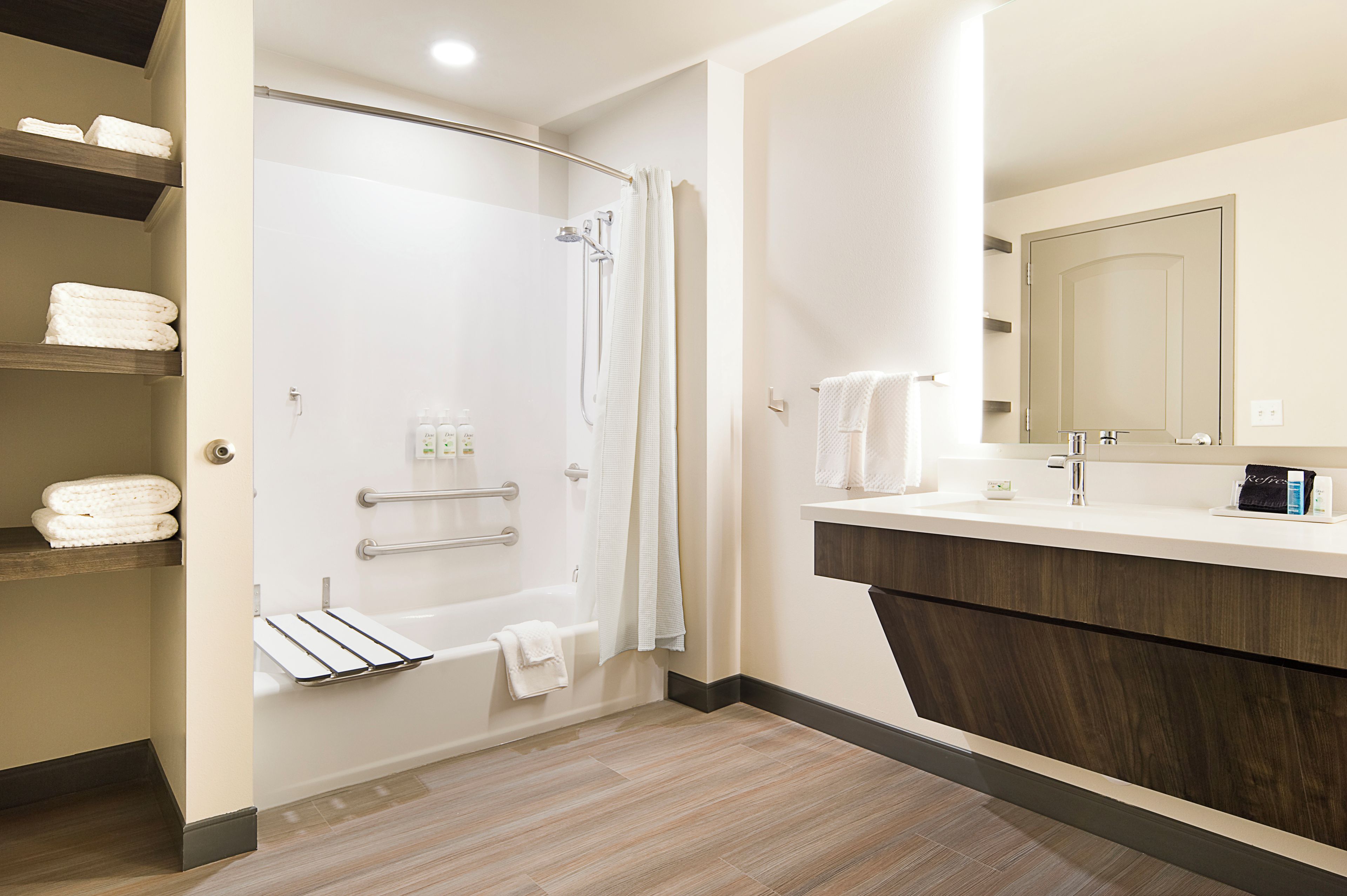 A modern bathroom with a shower, a bathtub, a vanity with a mirror, and shelves with towels.