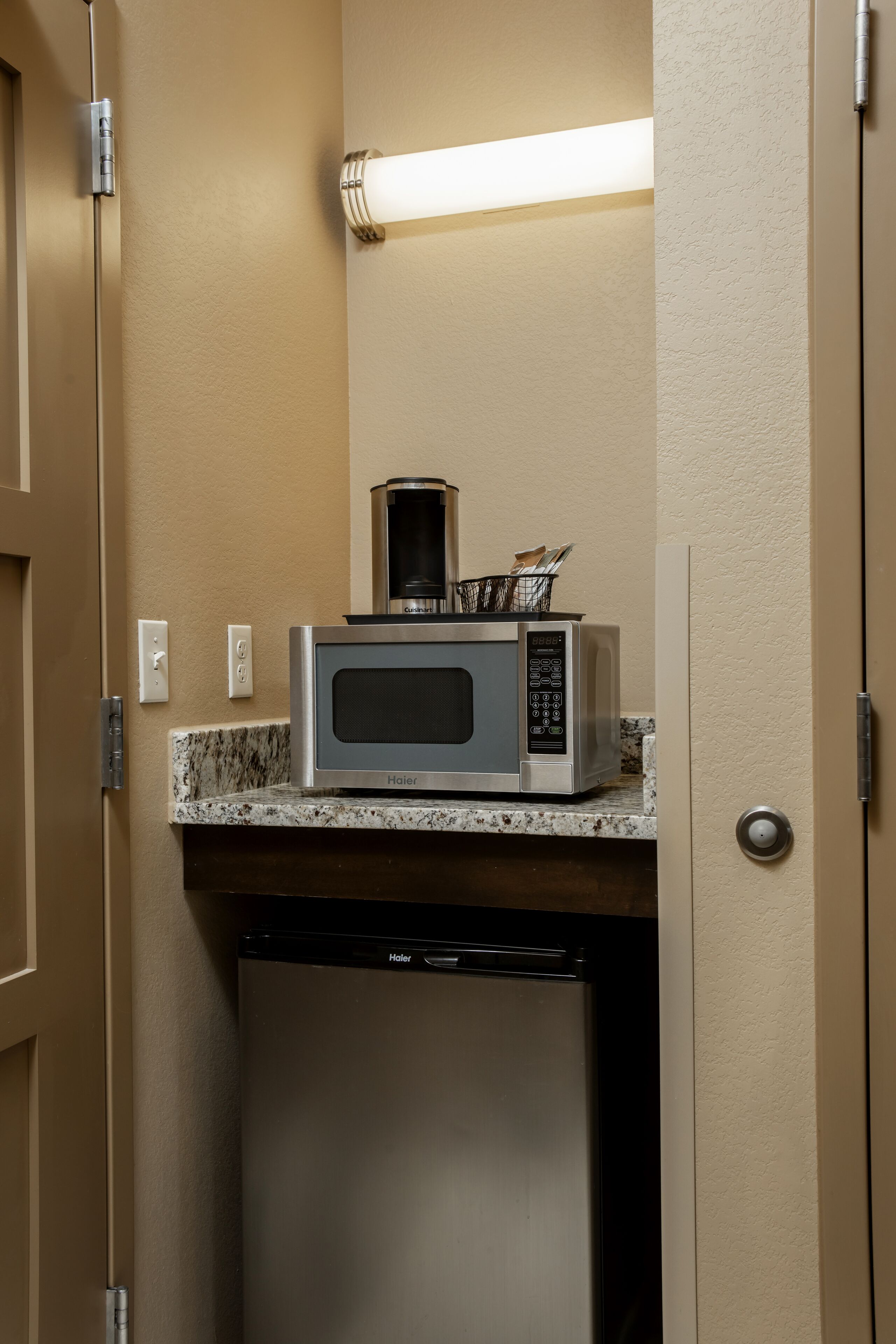 Una kitchenette compacta con microondas, cafetera y un refrigerador pequeño.