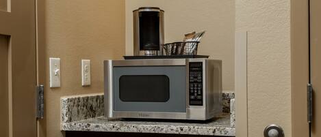 Una kitchenette compacta con microondas, cafetera y un refrigerador pequeño.
