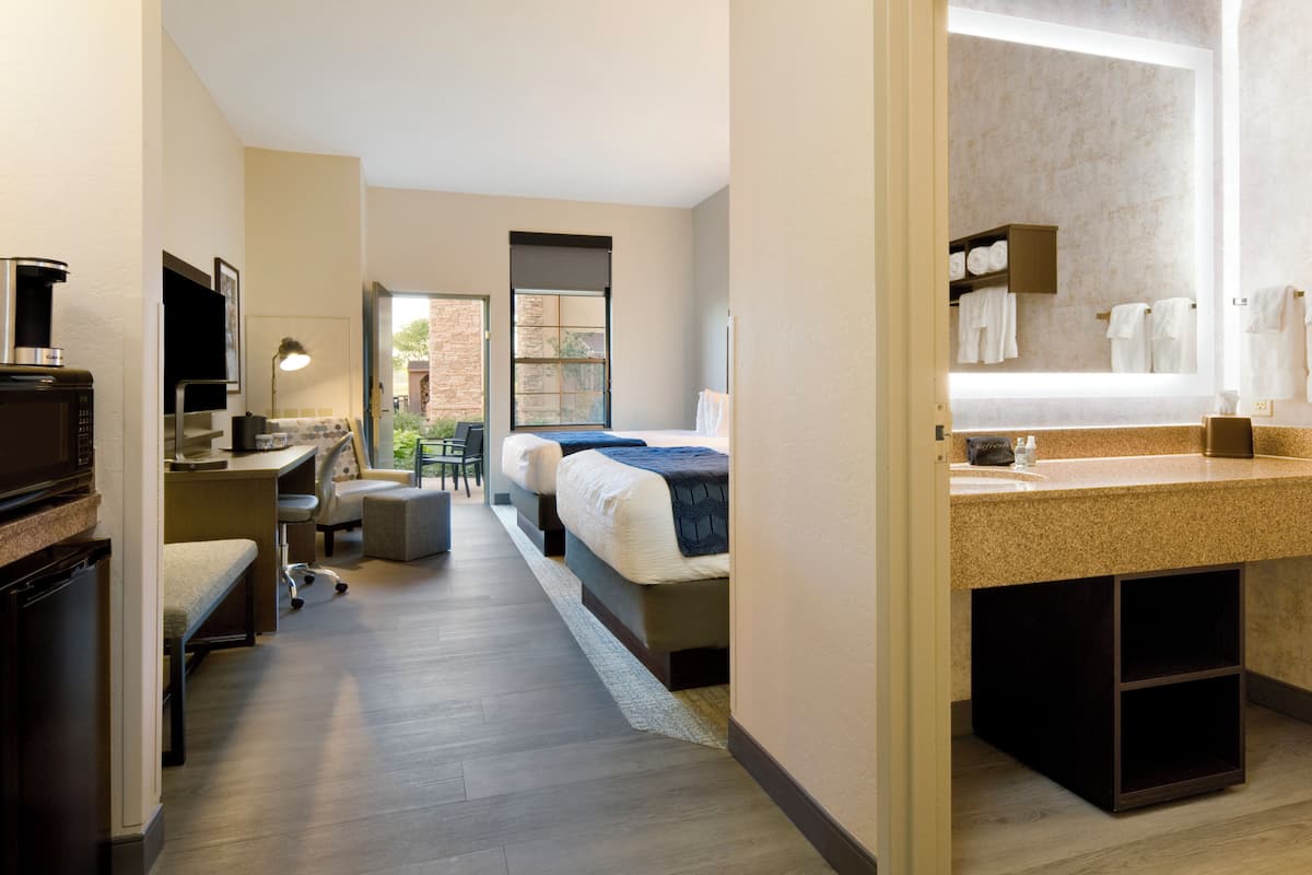 Une chambre d’hôtel comprenant un lit, un bureau, une chaise et une salle de bain avec un lavabo et un miroir.