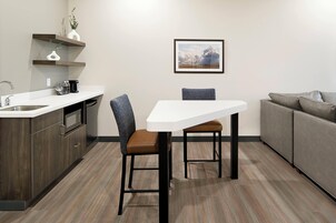 Une cuisine moderne avec un plan de travail blanc, des meubles de cuisine en bois foncé, un canapé gris et un tableau encadré au mur.