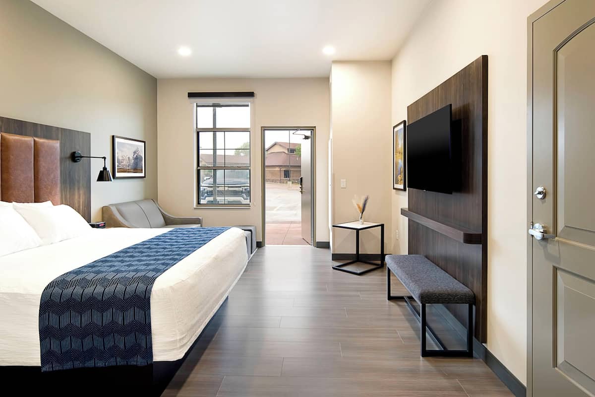 Une chambre d’hôtel avec un lit, un banc, une télévision et une porte.