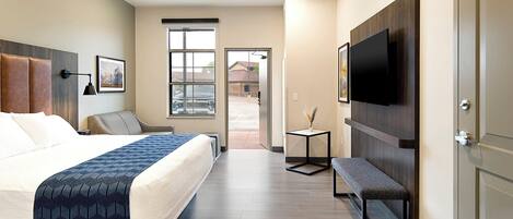 A hotel room with a bed, a bench, a TV, and a door.