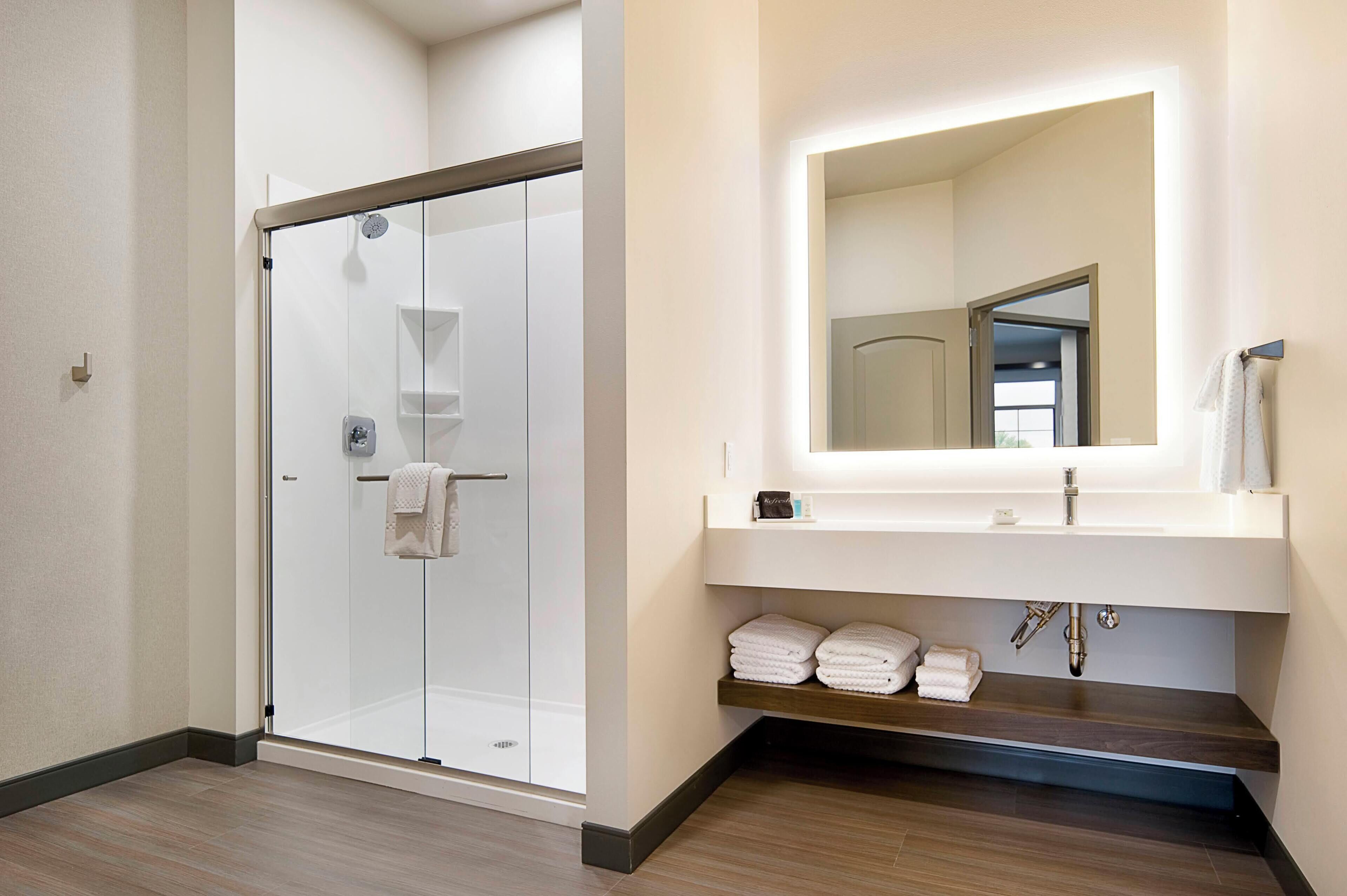 Une salle de bain moderne avec une douche à parois de verre, un grand miroir et un meuble-lavabo en bois.