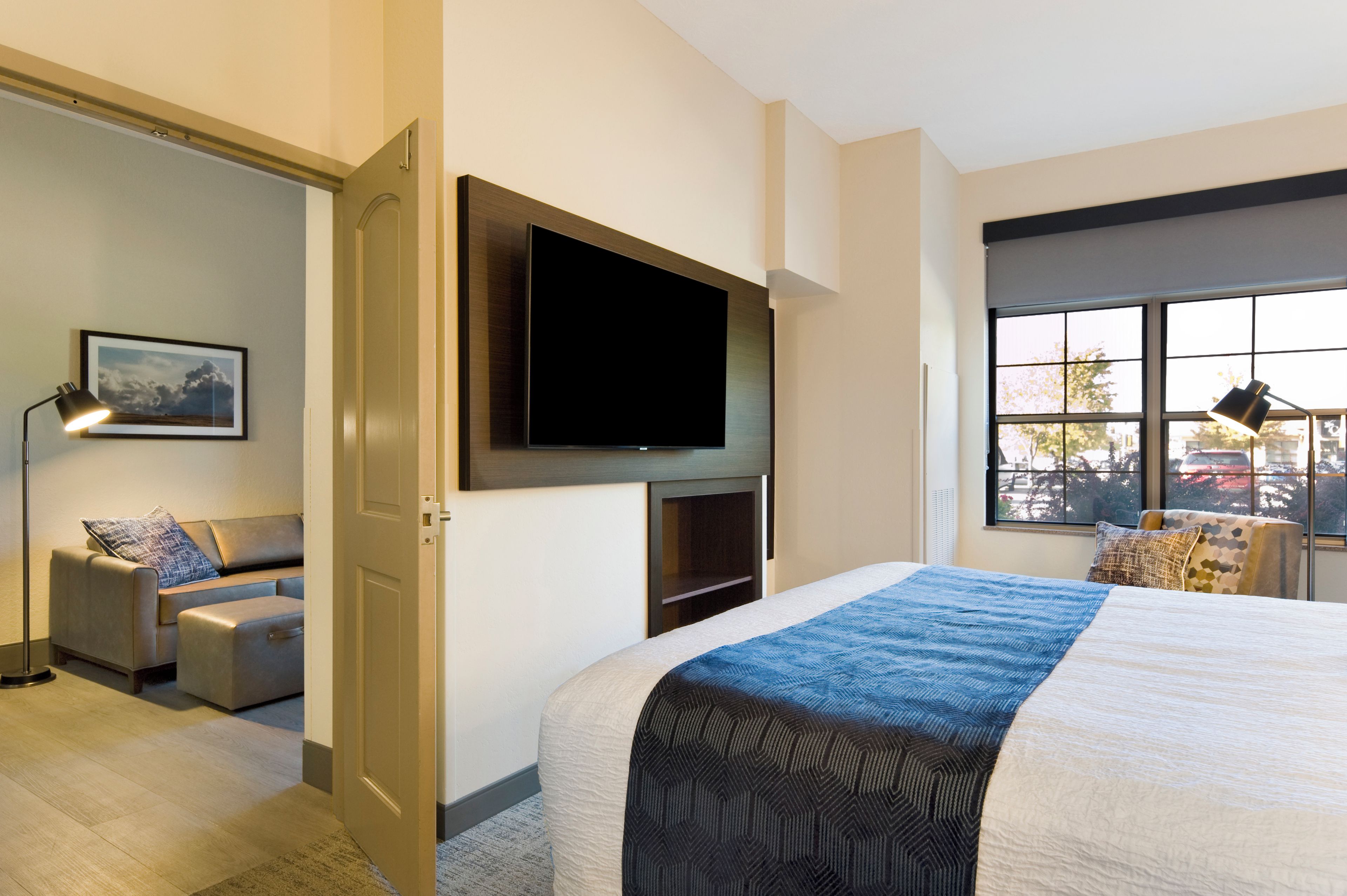 A hotel room with a bed, a television mounted on the wall, a sofa, and a window with a view of the outside.