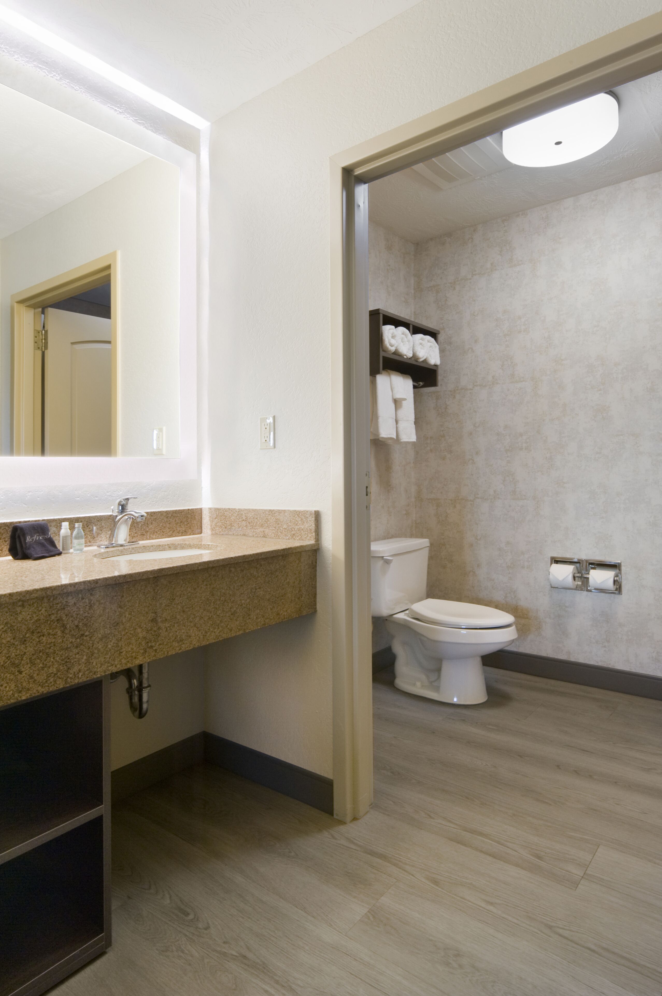 A modern bathroom with a granite countertop, a large mirror, a toilet, and a shower area.