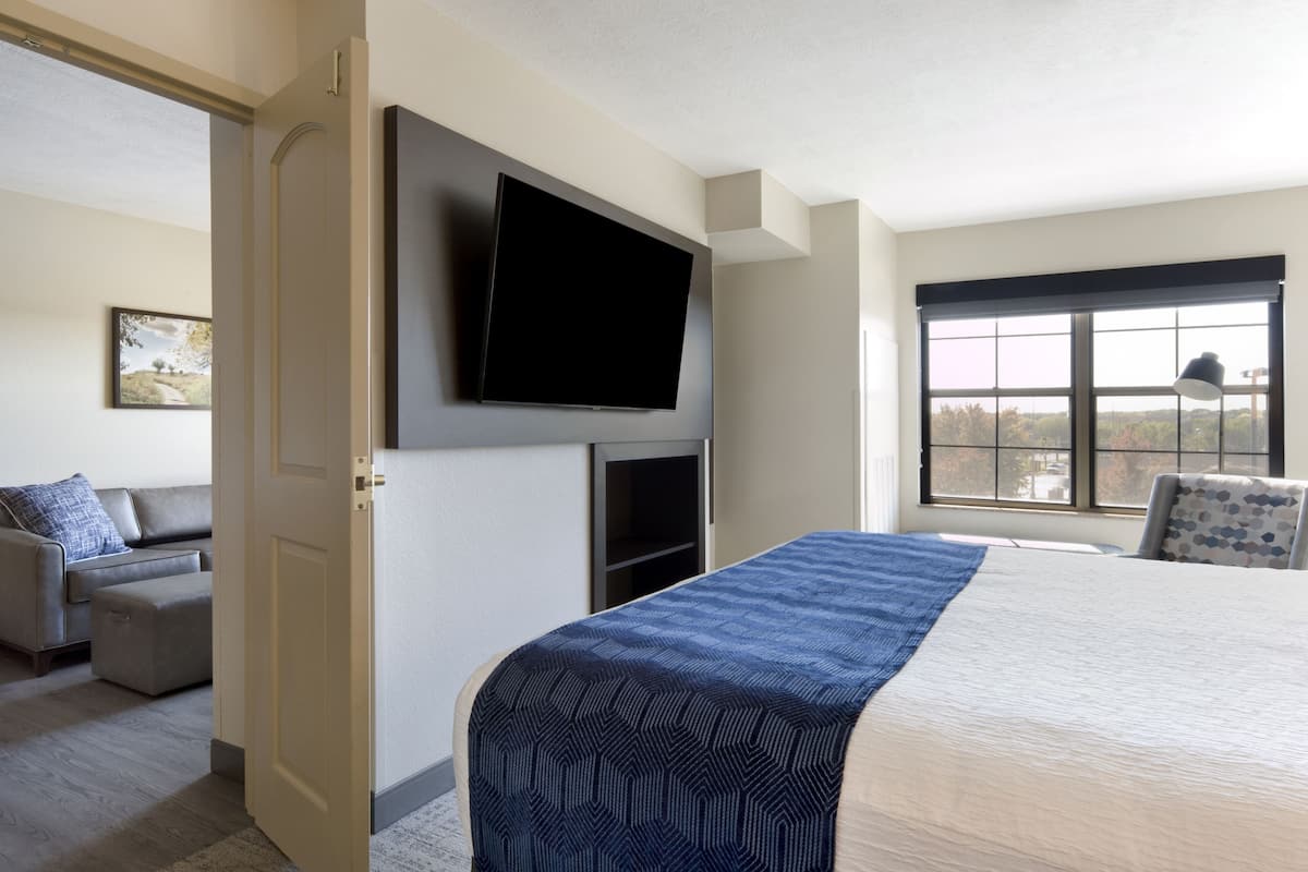 Une chambre d’hôtel dotée d’un grand lit, d’un téléviseur à écran plat fixé au mur, d’une fenêtre offrant une vue agréable et d’un coin salon avec un canapé et un pouf.
