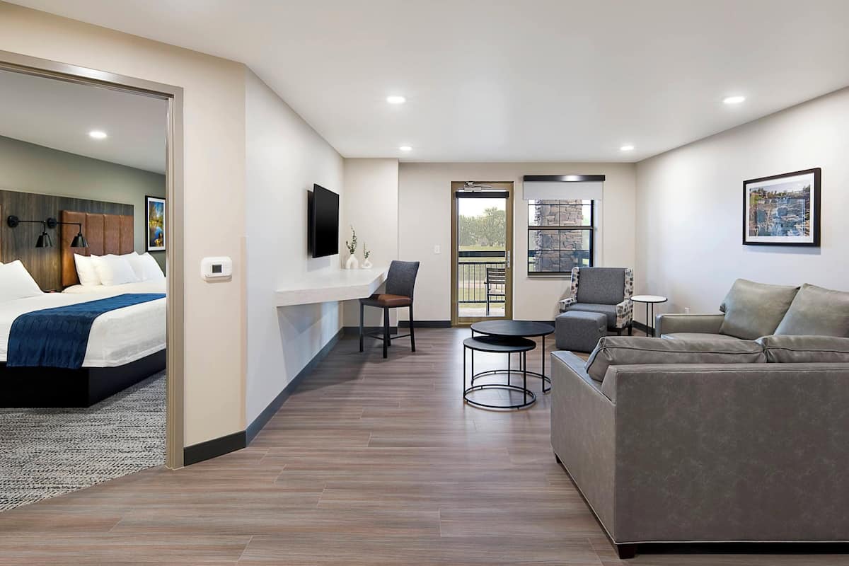 Une chambre d’hôtel moderne comprenant un lit, un coin salon avec un canapé et des fauteuils, une petite table et un balcon doté d’une balustrade.