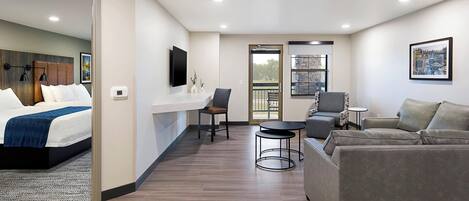 Habitación de hotel moderna con cama, zona de estar con sofá y sillones, una mesita y un balcón con barandilla.